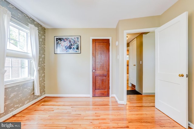 unfurnished room with wallpapered walls, baseboards, and light wood-type flooring