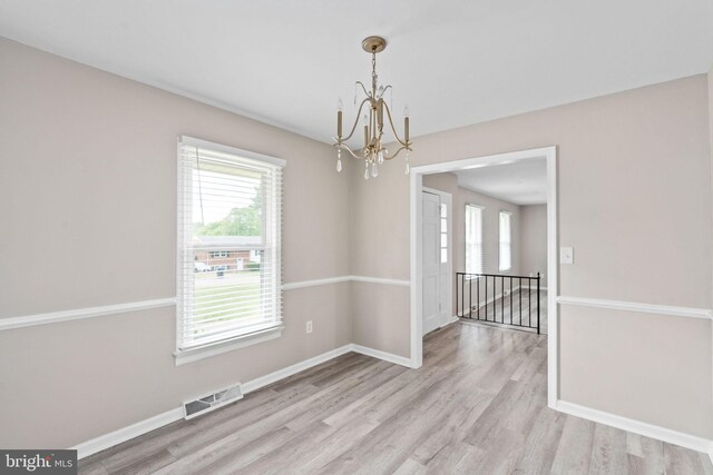 unfurnished dining area with an inviting chandelier, plenty of natural light, visible vents, and light wood-type flooring