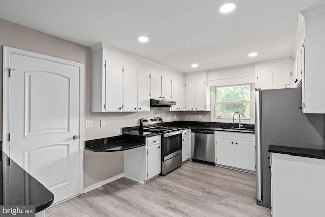 kitchen featuring dark countertops, appliances with stainless steel finishes, a sink, light wood-style flooring, and white cabinetry