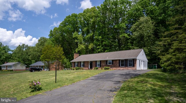 ranch-style home featuring brick siding, a chimney, a front lawn, and aphalt driveway