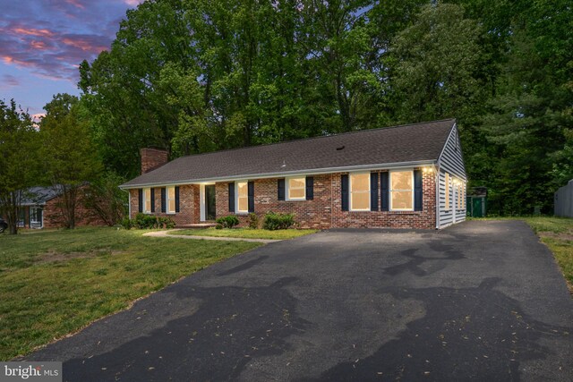 ranch-style house with a shingled roof, brick siding, a front yard, a chimney, and driveway