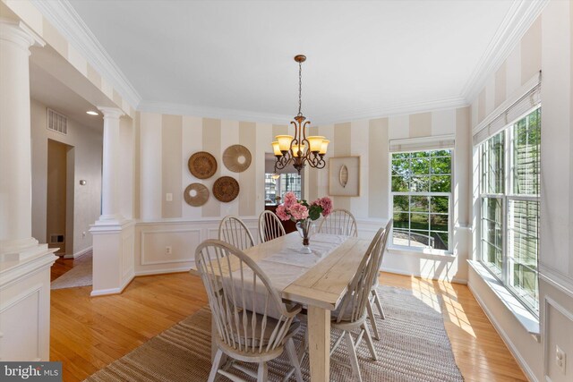 dining room featuring ornate columns, ornamental molding, light wood-style floors, and wallpapered walls