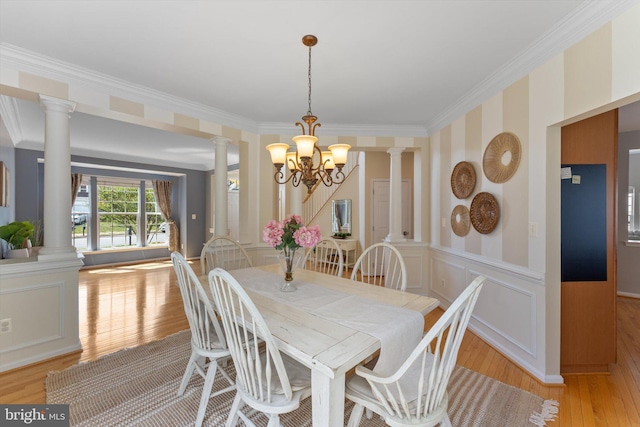 dining space featuring decorative columns, light wood-type flooring, an inviting chandelier, ornamental molding, and a decorative wall