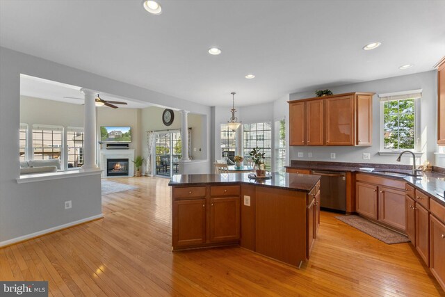 kitchen featuring ceiling fan, a center island, dishwasher, a sink, and a glass covered fireplace