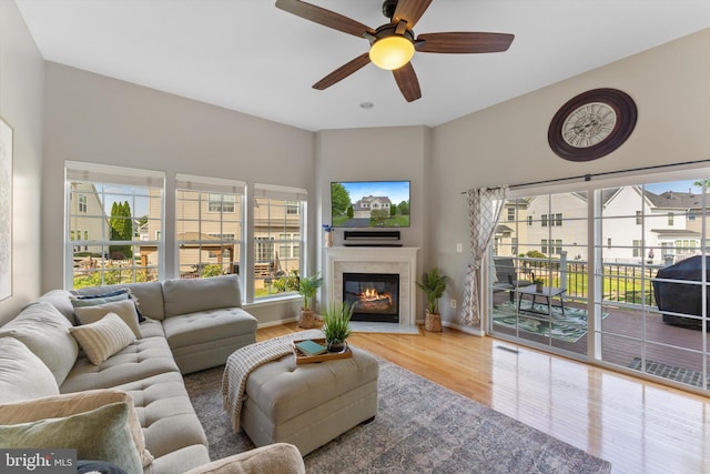 living room featuring a glass covered fireplace, baseboards, ceiling fan, and wood finished floors