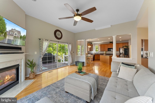 living room featuring ceiling fan, decorative columns, light wood-style flooring, and a high end fireplace