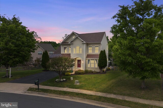 traditional-style house with a standing seam roof, driveway, metal roof, a lawn, and fence