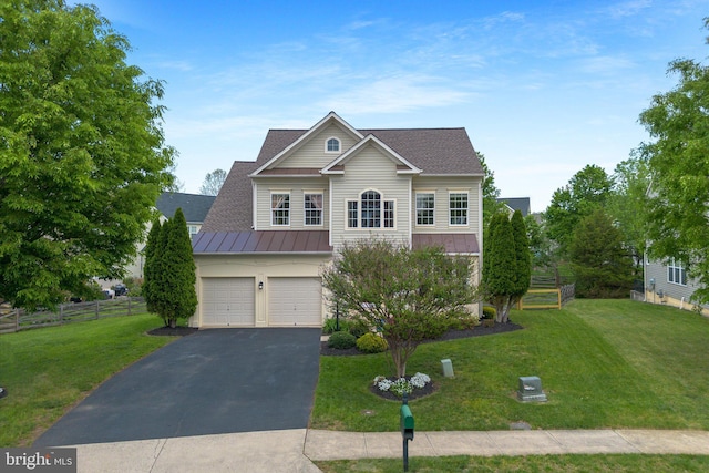 traditional-style house with fence, a front yard, a standing seam roof, an attached garage, and driveway