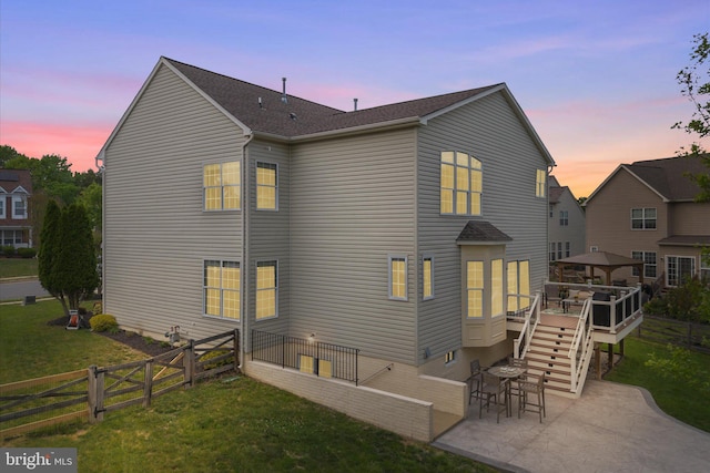 back of house at dusk with stairs, a deck, a fenced backyard, a patio area, and a lawn