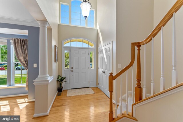 foyer entrance with decorative columns, a towering ceiling, stairway, baseboards, and light wood finished floors