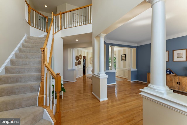 entrance foyer featuring crown molding, decorative columns, light wood-style flooring, and stairway