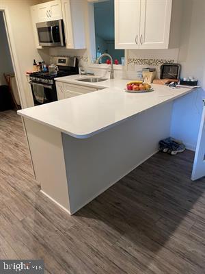 25 Bucknell Rd, Somers Point, NJ 08244 - kitchen with appliances with stainless steel finishes, wood finished floors, a sink, white cabinetry, and a peninsula