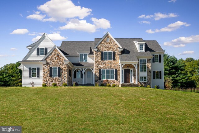shingle-style home with roof with shingles, a front yard, and stone siding