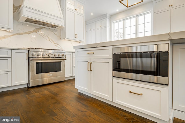 kitchen featuring custom exhaust hood, high end stainless steel range, light stone countertops, white cabinets, and dark wood finished floors