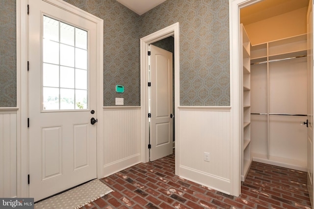 doorway to outside with brick floor, a wainscoted wall, and wallpapered walls