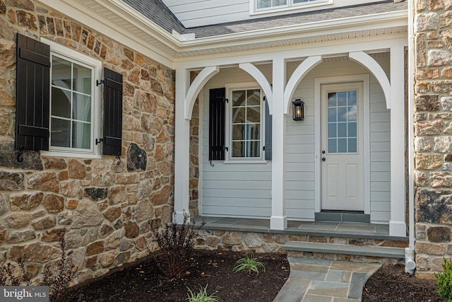 property entrance with roof with shingles, covered porch, and stone siding