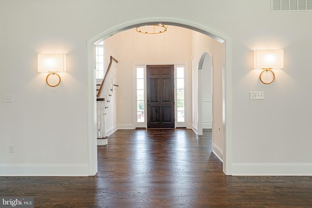 entryway featuring visible vents, arched walkways, stairway, baseboards, and dark wood-style floors