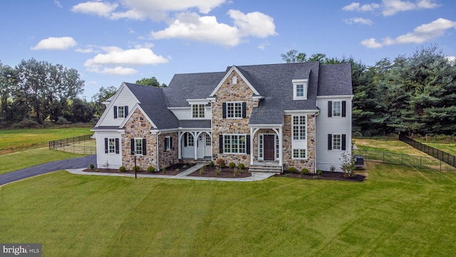 shingle-style home with fence, a front yard, and stone siding