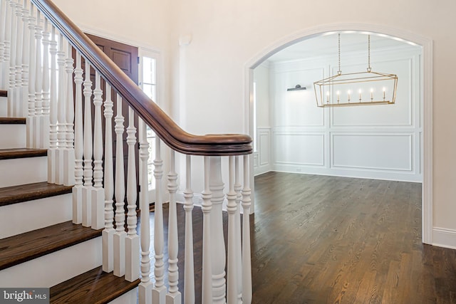 stairs featuring arched walkways, wood finished floors, and a decorative wall