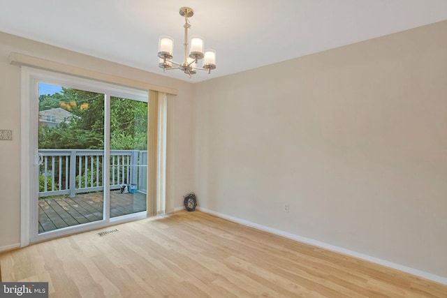 empty room featuring baseboards, a chandelier, wood finished floors, and visible vents