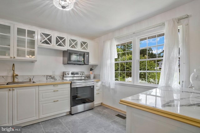 kitchen with glass insert cabinets, light countertops, white cabinetry, a sink, and appliances with stainless steel finishes