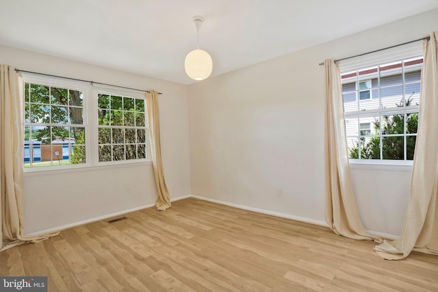 unfurnished room featuring visible vents, light wood-style flooring, baseboards, and a wealth of natural light