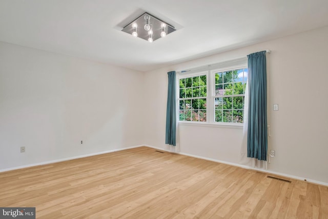unfurnished room featuring baseboards, visible vents, wood finished floors, and an inviting chandelier