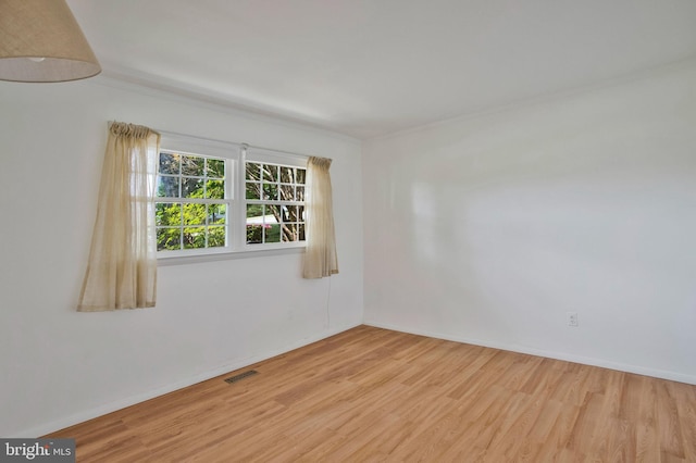 spare room with crown molding, baseboards, visible vents, and wood finished floors