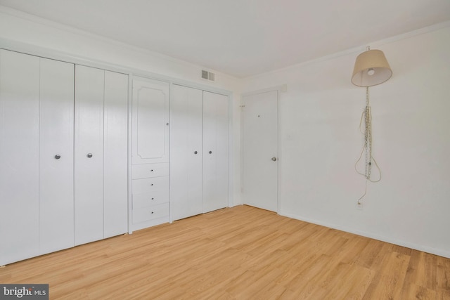unfurnished bedroom featuring visible vents, light wood-style flooring, and multiple closets