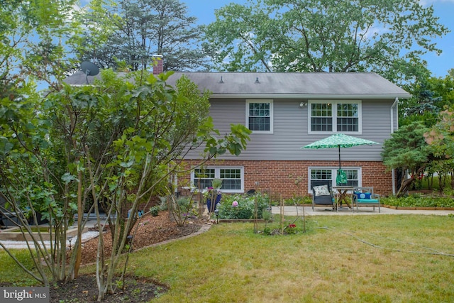 back of house featuring brick siding, a patio area, a yard, and a chimney