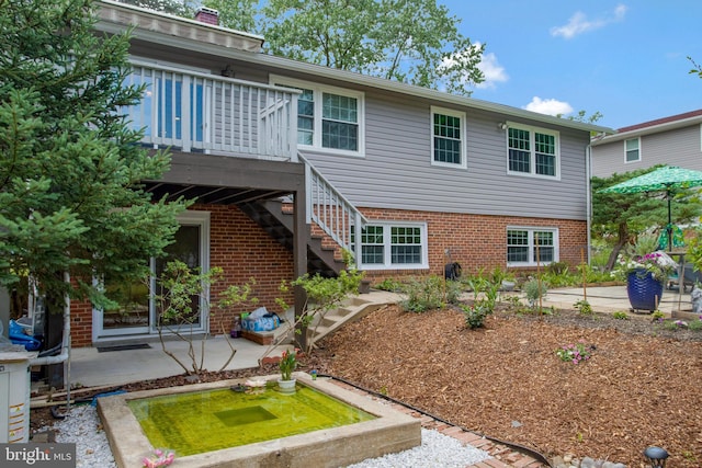 rear view of house with a wooden deck, a patio area, and brick siding