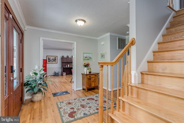 foyer entrance with a textured ceiling, visible vents, wood finished floors, baseboards, and stairs