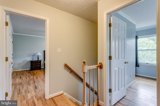 hallway featuring baseboards, an upstairs landing, ornamental molding, and light wood-style floors