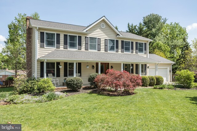 colonial inspired home with a front yard, a chimney, a shingled roof, an attached garage, and a porch