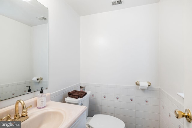 bathroom featuring toilet, visible vents, wainscoting, and tile walls