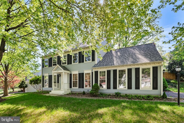 colonial house featuring a shingled roof and a front yard