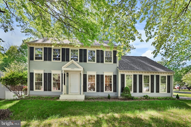 colonial home featuring a shingled roof and a front lawn