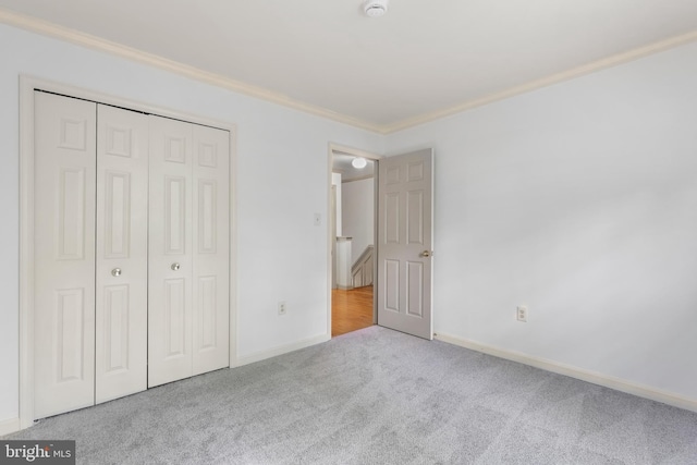 unfurnished bedroom featuring crown molding, baseboards, carpet, and a closet