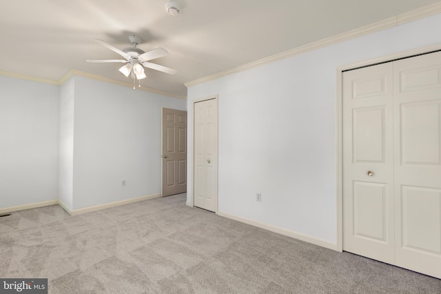 unfurnished bedroom with carpet floors, ornamental molding, baseboards, and two closets