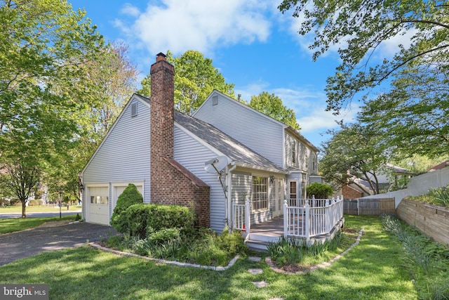 view of property exterior with a chimney, a deck, fence, aphalt driveway, and a yard