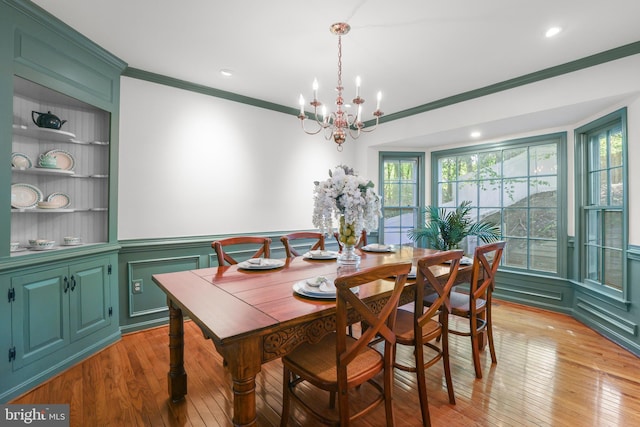 dining space featuring light wood-type flooring, ornamental molding, a notable chandelier, and built in shelves