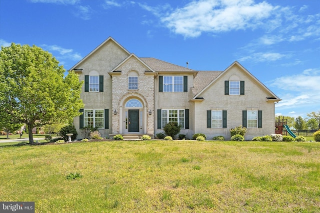 colonial inspired home featuring a playground, a front yard, and stucco siding