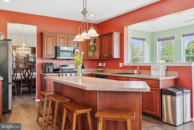 kitchen featuring decorative light fixtures, appliances with stainless steel finishes, a sink, light countertops, and light wood finished floors
