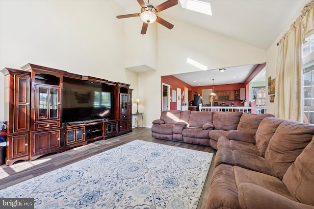 living area with high vaulted ceiling, a ceiling fan, baseboards, wood finished floors, and a skylight