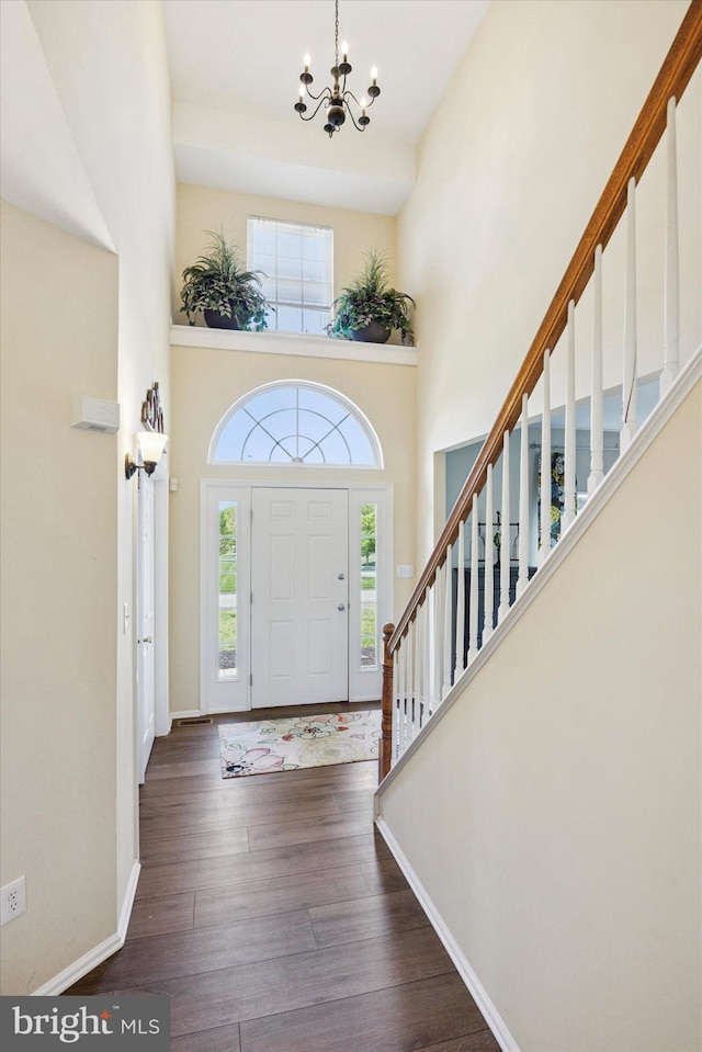 entrance foyer with baseboards, an inviting chandelier, wood finished floors, and a towering ceiling