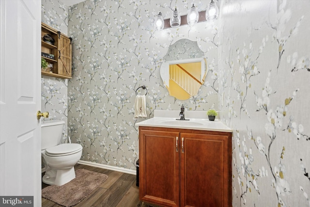 bathroom featuring vanity, toilet, baseboards, wallpapered walls, and wood finished floors