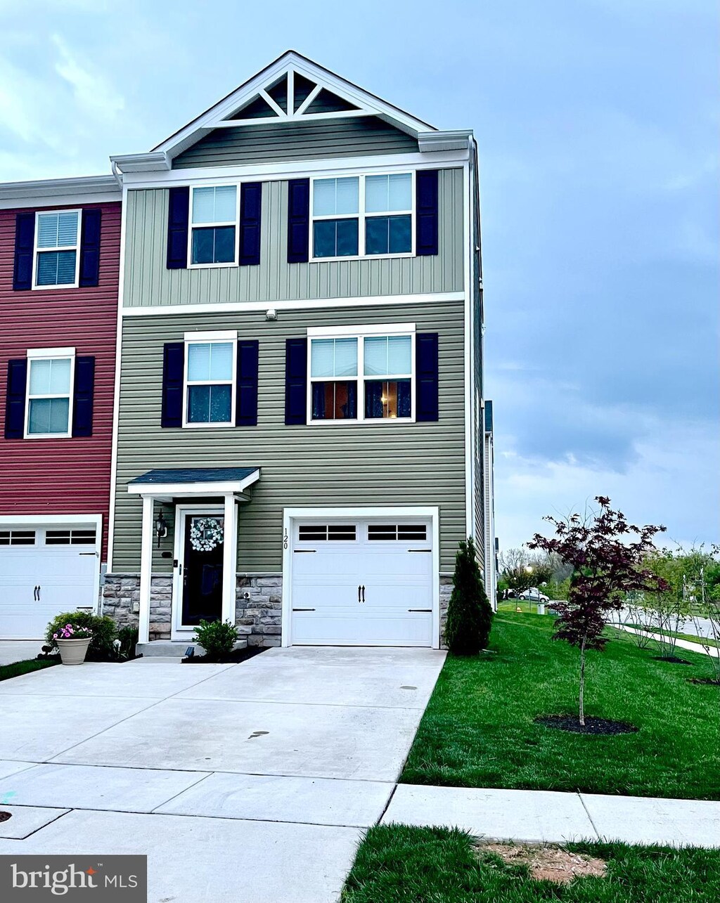 townhome / multi-family property featuring an attached garage, stone siding, board and batten siding, a front yard, and driveway