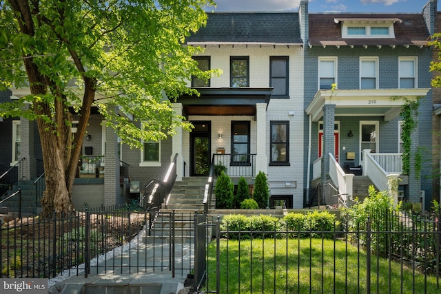 multi unit property featuring brick siding, a fenced front yard, stairway, and a porch