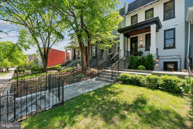 view of front of house with a front lawn, fence, covered porch, brick siding, and stairs