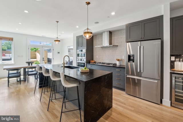 kitchen with beverage cooler, wall chimney range hood, tasteful backsplash, a sink, and appliances with stainless steel finishes
